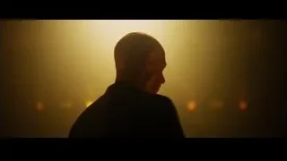 bald man speaking into microphone on stage — Whiplash