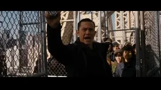 man holding gun behind chain-link fence — Batman: The Dark Knight Rises