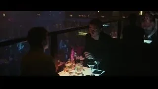 People at dimly lit bar with city skyline — The Social Network