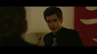 young man in suit before red wall — The Social Network