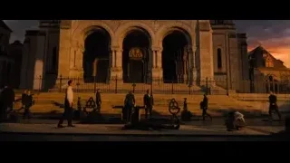 People gathered at ornate building with statue at sunset — John Wick: Chapter 4