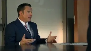 man in suit speaking into microphone at desk — Suits