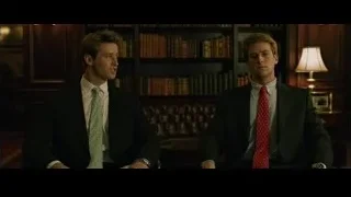 two young men in suits by bookshelf — The Social Network