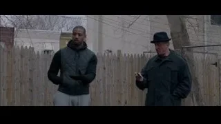 two men with gun by wooden fence — Creed