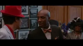 two men in suits talking in room with pictures — The Dictator