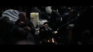 People sitting around campfire in dark room — Batman: The Dark Knight Rises