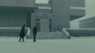 Two people walking in snow by modern building — Blade Runner 2049