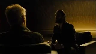 two men sitting on a couch in dimly lit room — Blade Runner 2049