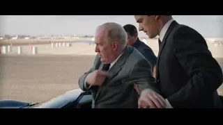 three men shaking hands by car at airport — Ford v Ferrari