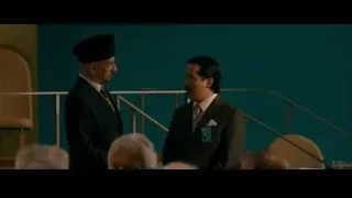 two men talking in room with blue wall — The Dictator