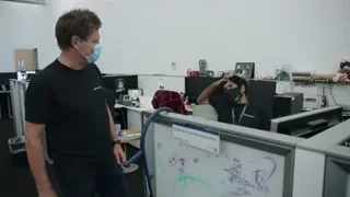 man in face mask pointing at whiteboard in cubicle — Elon Musk: Return to Space