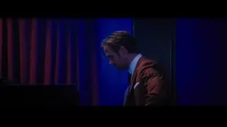 man in suit standing by piano and red curtain — La La Land
