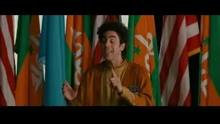 Man in golden robe speaking before flags — The Dictator