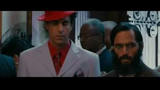 Man in red hat and suit conversing — The Dictator