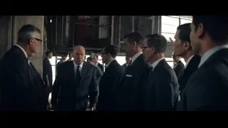 men in suits in dimly lit industrial space — Ford v Ferrari