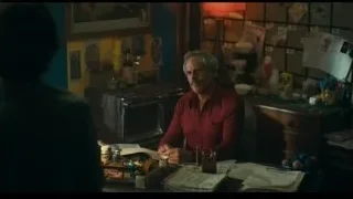 Man in red shirt at cluttered desk holding pen — Joker