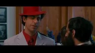 man in red hat white suit looking serious — The Dictator