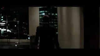 man in suit leaning by window with city view — Batman: The Dark Knight