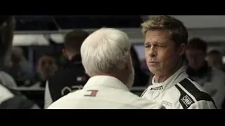 two men in racing suits talking in garage — F1