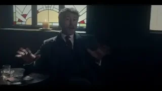 man gesturing at bar table with whiskey and cards — Peaky Blinders